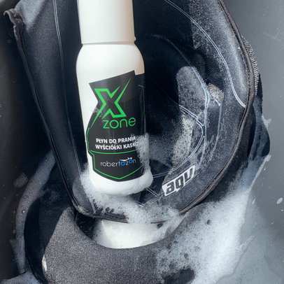 Butelka Xzone – płyn do prania wyściółki kasku, ustawiona na namydlonej wyściółce motocyklowego kasku w trakcie prania.