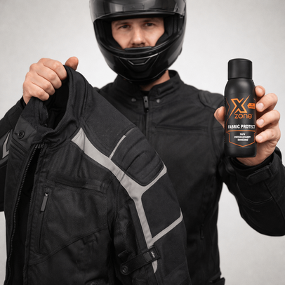 Motocyklista w kasku trzyma kurtkę motocyklową oraz spray Xzone Fabric Protect do ochrony tkanin, podkreślając pielęgnację i odświeżanie odzieży motocyklowej.