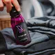 Butelka Xzone Active Care – płyn do prania odzieży termoaktywnej, trzymana w dłoni obok sportowych ubrań.